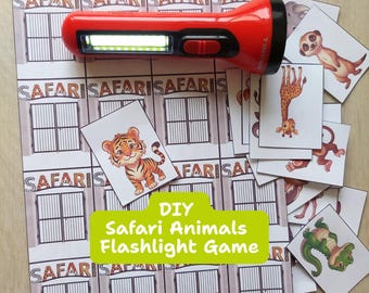 May include: A red plastic torch with a bright LED light positioned over a printed paper sheet featuring a grid of safari gate illustrations and several separate cards depicting cartoon animals like a tiger, giraffe, and crocodile.