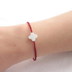 Könnte beinhalten: Ein rotes Perlenarmband mit einem weißen vierblättrigen Kleeblatt-Anhänger.