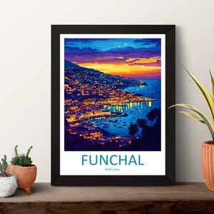 Op de afbeelding: Een ingelijste kunstdruk van Funchal, Portugal, bij zonsondergang. De afbeelding toont een kuststad met lichten die weerspiegelen op het water, onder een kleurrijke lucht. De print zit in een zwart frame, met de naam van de stad onderaan.