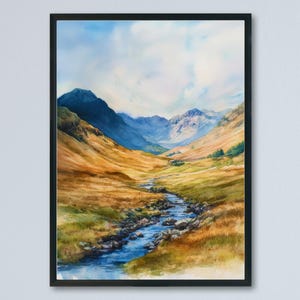 May include: A framed watercolor painting of a mountain landscape. The artwork depicts a valley with a river flowing through it, surrounded by rolling hills and mountains in shades of blue, green, and gold. The sky is a mix of blue and white.
