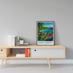 May include: A framed poster with a colorful illustration of a tropical island scene. The poster is titled "Saint Barts, Caribbean". The poster is displayed on a wooden shelf with books and a small potted plant.