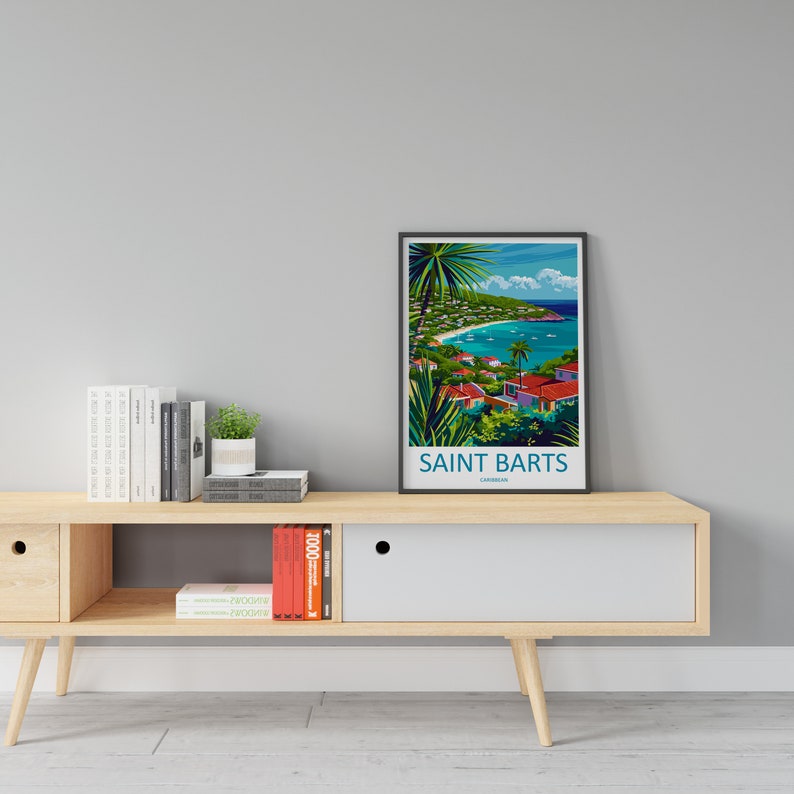 May include: A framed poster with a colorful illustration of a tropical island scene. The poster is titled "Saint Barts, Caribbean". The poster is displayed on a wooden shelf with books and a small potted plant.