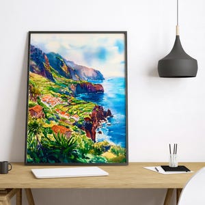 Pode incluir: Pintura em aquarela de uma paisagem costeira com fal&eacute;sias, oceano e edif&iacute;cios. A obra apresenta azuis, verdes e laranjas vibrantes, emoldurados em preto. A cena retrata um dia ensolarado com vista para o mar.