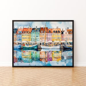May include: Watercolor painting of a waterfront scene with colorful buildings and boats. The buildings have red, orange, yellow, green, and pink facades. Boats are docked in the water, reflecting the buildings. The artwork is framed in a black frame.