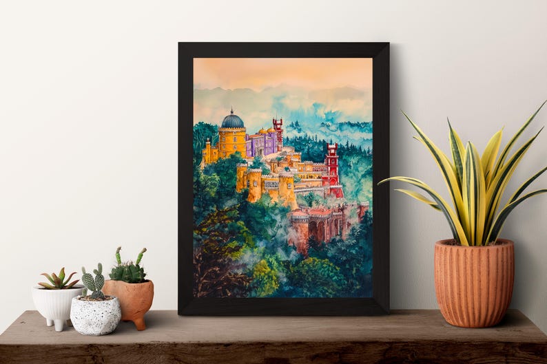 May include: A framed watercolor painting of a colorful castle complex nestled in a lush, green landscape. The artwork features buildings in shades of yellow, red, and purple, set against a backdrop of blue and green hills.