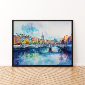 May include: Watercolour painting of a European city with a bridge over a river. The artwork shows buildings in orange, yellow, and brown, with a blue sky and water. The painting is framed in a black frame.