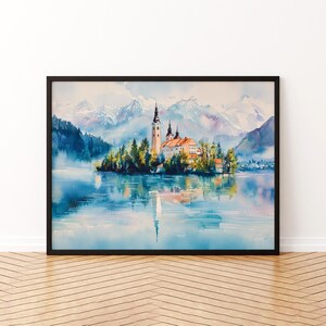 Può includere: Dipinto ad acquerello incorniciato in nero di una chiesa su un'isola in un lago. L'opera raffigura un paesaggio sereno con montagne innevate che si riflettono nell'acqua blu. Gli alberi circondano l'isola.