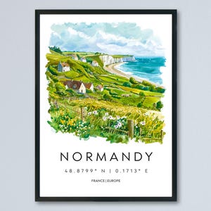 Puede incluir: Una impresión en acuarela enmarcada de la costa de Normandía. La obra representa acantilados verdes, casas blancas, una playa de arena y el océano bajo un cielo azul. La palabra "NORMANDY" está impresa debajo, junto con coordenadas y "FRANCE | EUROPE".