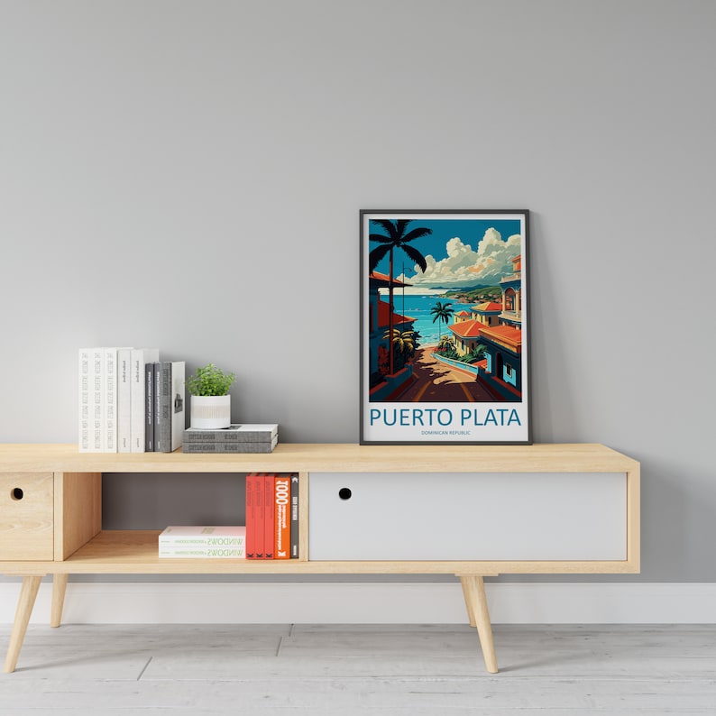 May include: A framed poster featuring a colourful illustration of a tropical beach scene in Puerto Plata, Dominican Republic. The poster is on a wooden shelf with books and a potted plant.