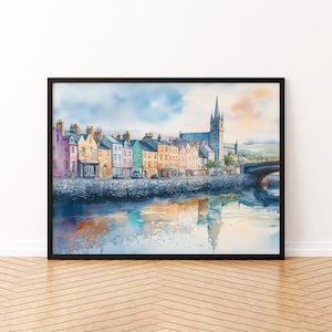May include: Watercolor print of a colorful European town with buildings in shades of pink, yellow, green, and blue. A church with a tall steeple is in the background. The image is framed in a black frame and reflects in the water.