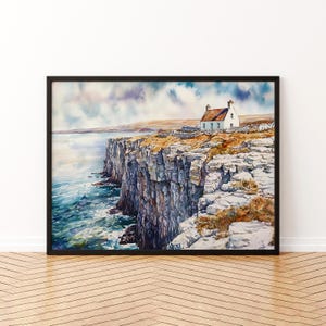 May include: Watercolour painting of a white cottage with a red roof on a cliff overlooking the sea. The artwork is framed in a black frame and depicts a dramatic coastal landscape with blue water and a cloudy sky.