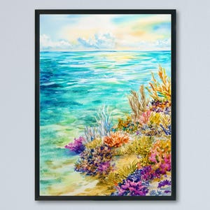 Op de afbeelding: Aquarel schilderij van een levendig zeegezicht in een zwarte lijst. Het kunstwerk toont een turquoise oceaan die een kleurrijk koraalrif ontmoet. De lucht gaat over van geel naar blauw, waardoor een serene kustscène ontstaat.
