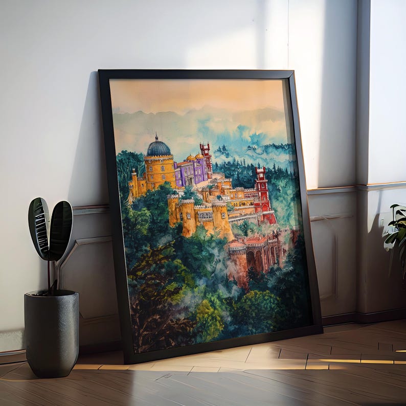 May include: Watercolor painting of a colorful castle on a hillside, framed in black. The artwork depicts a vibrant scene with yellow, purple, and red buildings surrounded by lush green trees and a blue sky. The framed art is leaning against a white wall.