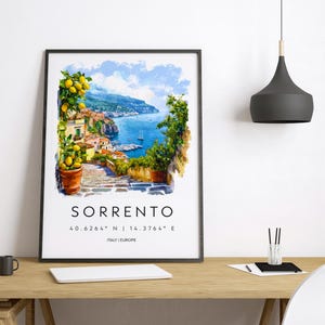 Puede incluir: Una impresi&oacute;n art&iacute;stica enmarcada de Sorrento, Italia, con una pintura de acuarela de un pueblo costero con mar azul, barcos y vegetaci&oacute;n. La impresi&oacute;n incluye el nombre de la ciudad y las coordenadas. El marco es negro.