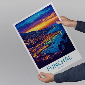 Op de afbeelding: Een print van Funchal, Portugal, met een kleurrijke weergave van de stad in de schemering. Het kunstwerk toont een levendige zonsondergang boven de stad, met het woord "FUNCHAL" in turquoise onderaan. De print wordt door een persoon vastgehouden.