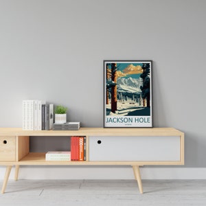 May include: A framed poster featuring a vintage illustration of a snowy mountain landscape. The poster is titled "Jackson Hole, Wyoming". The poster is displayed on a light wood shelf with books and a small potted plant.