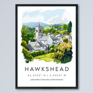 May include: Framed art print of Hawkshead, England, featuring a watercolor illustration of a village with a church steeple, surrounded by green trees and rolling hills. The print includes the town's name and coordinates.