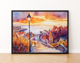 May include: Watercolor painting of a coastal town at sunset. The artwork features a street with steps leading down to the water, lined with buildings with red roofs. A black framed print with a lamppost in the foreground.