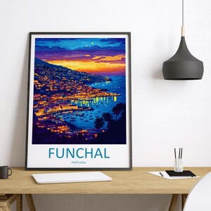 Op de afbeelding: Een ingelijste kunstdruk van Funchal, Portugal, bij zonsondergang. De afbeelding toont een kuststad met gebouwen verlicht door warme lichten, tegen een levendige lucht van oranje, geel en blauw. Het woord "FUNCHAL" staat onderaan afgedrukt.