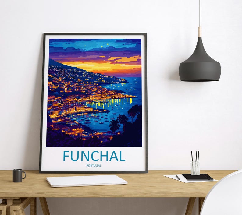 Op de afbeelding: Een ingelijste kunstdruk van Funchal, Portugal, bij zonsondergang. De afbeelding toont een kuststad met gebouwen verlicht door warme lichten, tegen een levendige lucht van oranje, geel en blauw. Het woord "FUNCHAL" staat onderaan afgedrukt.