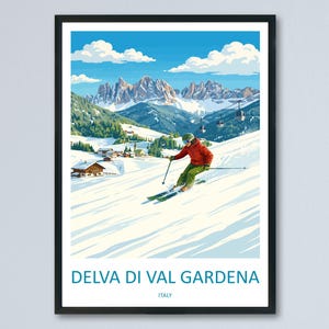 May include: Framed vintage travel poster featuring a skier on a snowy slope in Delva di Val Gardena, Italy. The poster has a black frame and depicts a mountain range, blue sky, and small buildings. The skier wears a red jacket and green pants.
