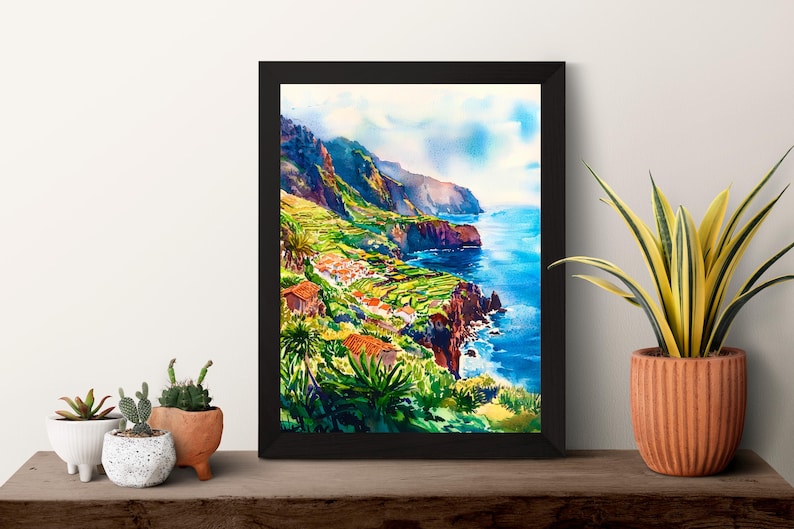Pode incluir: Uma pintura em aquarela emoldurada retrata uma paisagem costeira com fal&eacute;sias, edif&iacute;cios e o oceano. A obra de arte apresenta cores vibrantes, incluindo azuis, verdes e laranjas. A pintura &eacute; exibida em uma superf&iacute;cie de madeira com plantas em vasos.