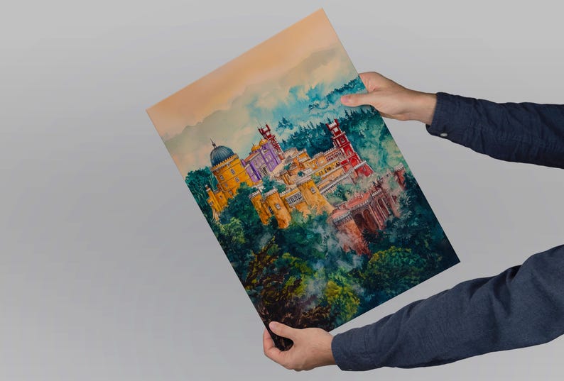 May include: A watercolor print of a colorful palace nestled in lush green trees. The artwork features a yellow dome, red towers, and purple accents. The print is held by a person wearing a dark blue long-sleeved shirt.