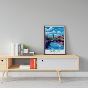 May include: A framed print of a colorful illustration of a cityscape with a bridge over a river. The text "DUBLIN, IRELAND" is at the bottom of the print. The print is on a wooden shelf with books and a potted plant.