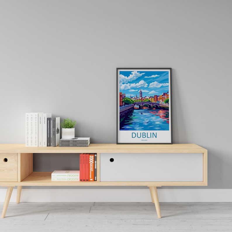 May include: A framed print of a colorful illustration of a cityscape with a bridge over a river. The text "DUBLIN, IRELAND" is at the bottom of the print. The print is on a wooden shelf with books and a potted plant.