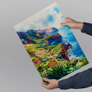 Pode incluir: Pintura em aquarela de uma paisagem costeira com vegeta&ccedil;&atilde;o verde exuberante, edif&iacute;cios com telhados vermelhos e uma fal&eacute;sia dram&aacute;tica. A obra apresenta azuis, verdes e castanhos vibrantes, capturando a ess&ecirc;ncia de uma vista panor&acirc;mica. A pintura &eacute; segurada por uma pessoa.