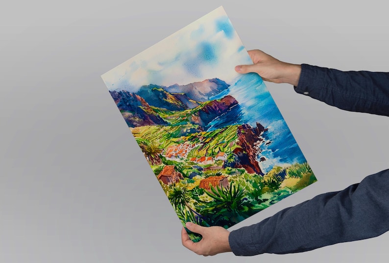 Pode incluir: Pintura em aquarela de uma paisagem costeira com vegeta&ccedil;&atilde;o verde exuberante, edif&iacute;cios com telhados vermelhos e uma fal&eacute;sia dram&aacute;tica. A obra apresenta azuis, verdes e castanhos vibrantes, capturando a ess&ecirc;ncia de uma vista panor&acirc;mica. A pintura &eacute; segurada por uma pessoa.