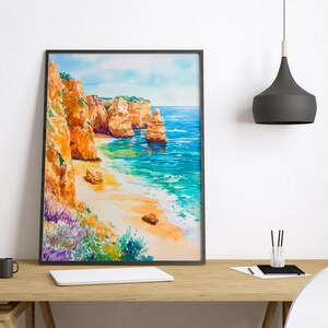 May include: A framed watercolor painting depicts a coastal scene with orange cliffs, a sandy beach, and turquoise water. The artwork features vibrant colors and a serene landscape, perfect for home decor.