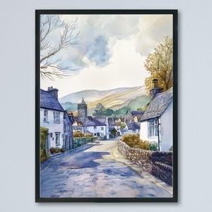 May include: Watercolor painting of a quaint village street framed in black. The artwork depicts white houses with blue roofs, a stone wall, and a church tower in the distance. The sky is a mix of blue and yellow.