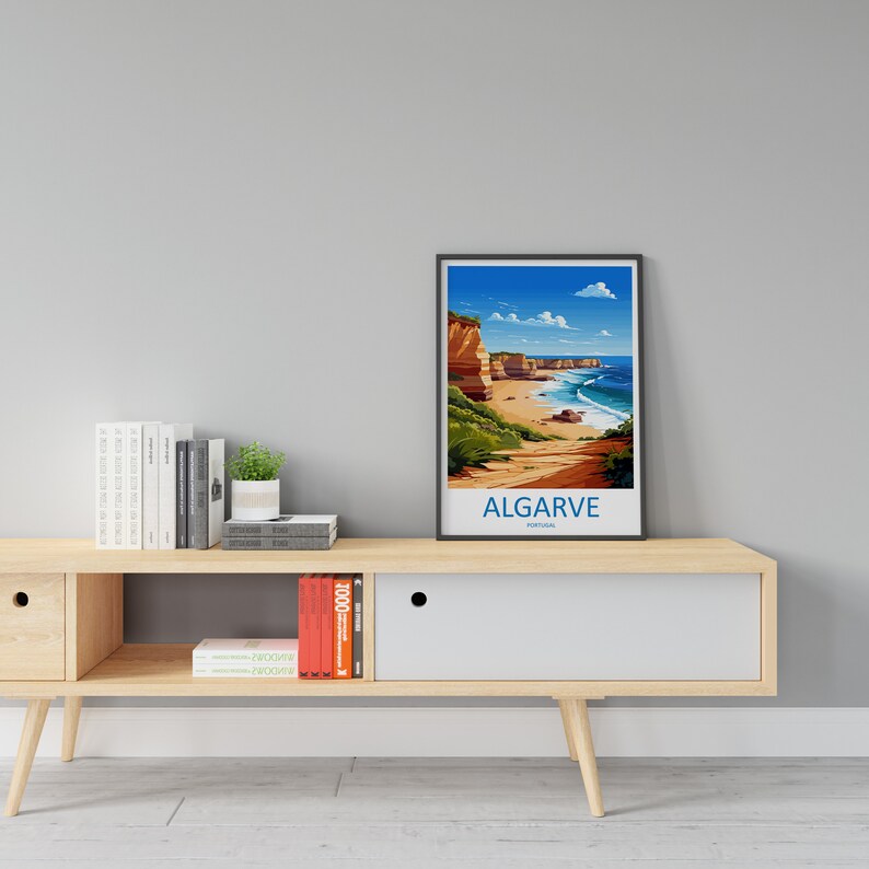 May include: A framed illustration of a coastal landscape with cliffs, a beach, and ocean waves. The text "ALGARVE PORTUGAL" is at the bottom of the image. The illustration is on a wooden shelf with books and a potted plant.