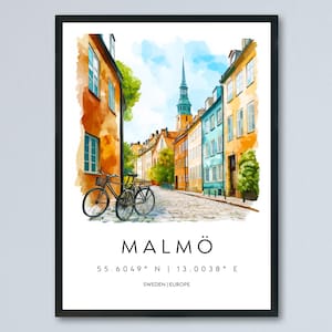Puede incluir: Impresión en acuarela de una escena callejera en Malmö, Suecia, con edificios coloridos y una bicicleta. La obra de arte incluye el nombre de la ciudad, las coordenadas y la ubicación. La impresión está enmarcada en un borde negro.