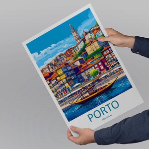 May include: A colorful art print of Porto, Portugal, featuring a detailed illustration of the city's waterfront with buildings, a boat, and the text "PORTO PORTUGAL". The print is held by a person.