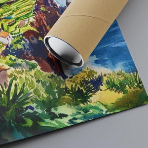 Pode incluir: Impress&atilde;o de arte em aquarela de paisagem com uma cena vibrante de colina com casas, &aacute;rvores e c&eacute;u azul. A obra de arte &eacute; enrolada em um tubo de papel&atilde;o marrom.