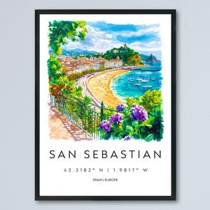 May include: Watercolor print of San Sebastian, Spain, in a black frame. The artwork depicts a coastal scene with a beach, buildings, and boats. Text at the bottom reads "SAN SEBASTIAN" and coordinates. The print includes vibrant colors and a scenic view.