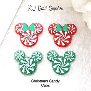 May include: Four Christmas candy cabochons in the shape of Mickey Mouse heads. Two are red and white with green bows, and two are green and white with green bows. The cabochons are made of resin and have a glitter finish.  RJ Bead Supplies - Christmas Candy Cabs
