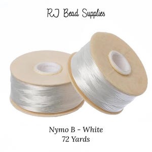May include: Two spools of white Nymo B thread, each containing 72 yards of thread. The spools are made of beige cardboard.