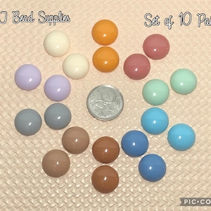 May include: Set of 10 pairs of round, colourful, plastic beads. The beads are arranged in a circle on a light pink surface. The text "Set of 10 Pairs" is at the top of the image.