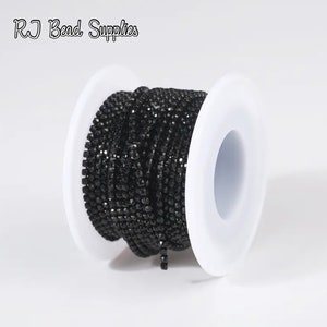 May include: A spool of black rhinestone chain. The chain is made of small, faceted rhinestones that are connected together to form a continuous chain.