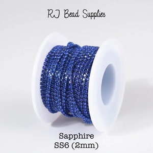 Peut inclure: Bobine de chaîne de strass bleu saphir, taille SS6 (2 mm). La chaîne est enroulée autour d'une bobine en plastique blanc.  RJ Bead Supplies est imprimé sur le fond blanc.