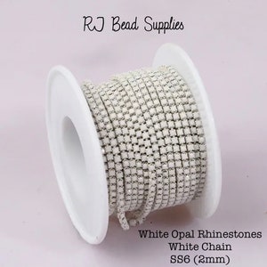 Peut inclure: Une bobine de chaîne de strass en opale blanche. La chaîne est composée de petits strass carrés. La chaîne mesure 2 mm de large et est étiquetée "White Opal Rhinestones White Chain SS6 (2mm)".