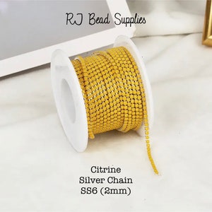 May include: A spool of yellow citrine silver chain, SS6 (2mm) in size. The chain is wound around a white spool. The chain is made of small, square-shaped beads.