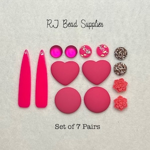 Peut inclure: Ensemble de sept paires de boucles d'oreilles roses et fuchsia. L'ensemble comprend des formes de cœur, rondes et florales. Le texte "Set of 7 Pairs" est imprimé sous les boucles d'oreilles.