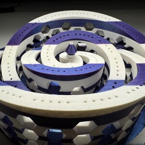 Peut inclure: Une sculpture abstraite imprimée en 3D avec un motif en spirale. La pièce présente des bandes blanches et bleues, avec un élément conique central. La structure a une apparence complexe et superposée avec des motifs géométriques et de petites perforations.