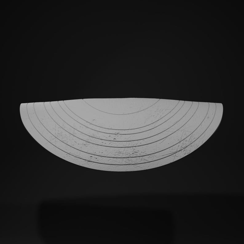 May include: A light gray, semi-circular object with concentric, textured lines. The object has a rough, weathered appearance and is set against a dark background. The design suggests a decorative or artistic piece.