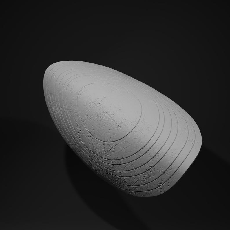 May include: A gray, oval-shaped sculpture with a textured surface and concentric circular grooves. The object is set against a dark background, highlighting its form and details. The sculpture's design suggests a modern or abstract aesthetic.