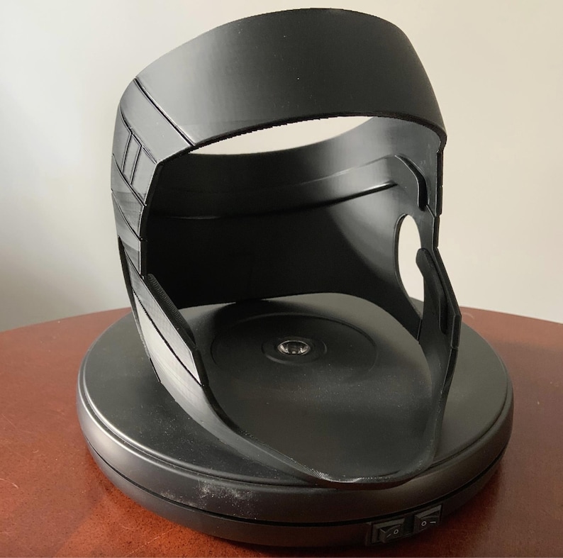 Puede incluir: Un casco de pl&aacute;stico negro con una base giratoria. El casco tiene una parte superior lisa y redondeada y un dise&ntilde;o texturizado y detallado en los lados.